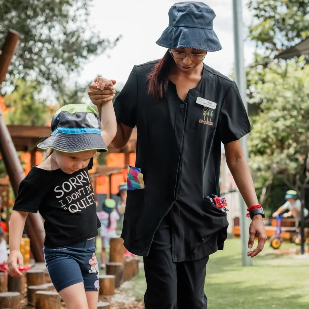 Educator walking hand in hand with a child through the outdoor play space
