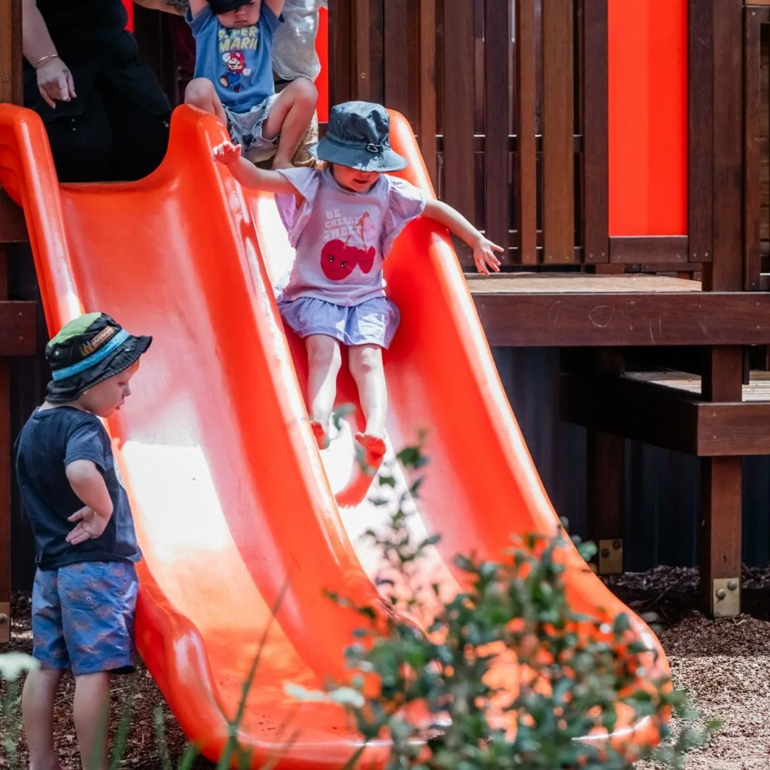 Children taking turns on the big orange slide in the playground fort