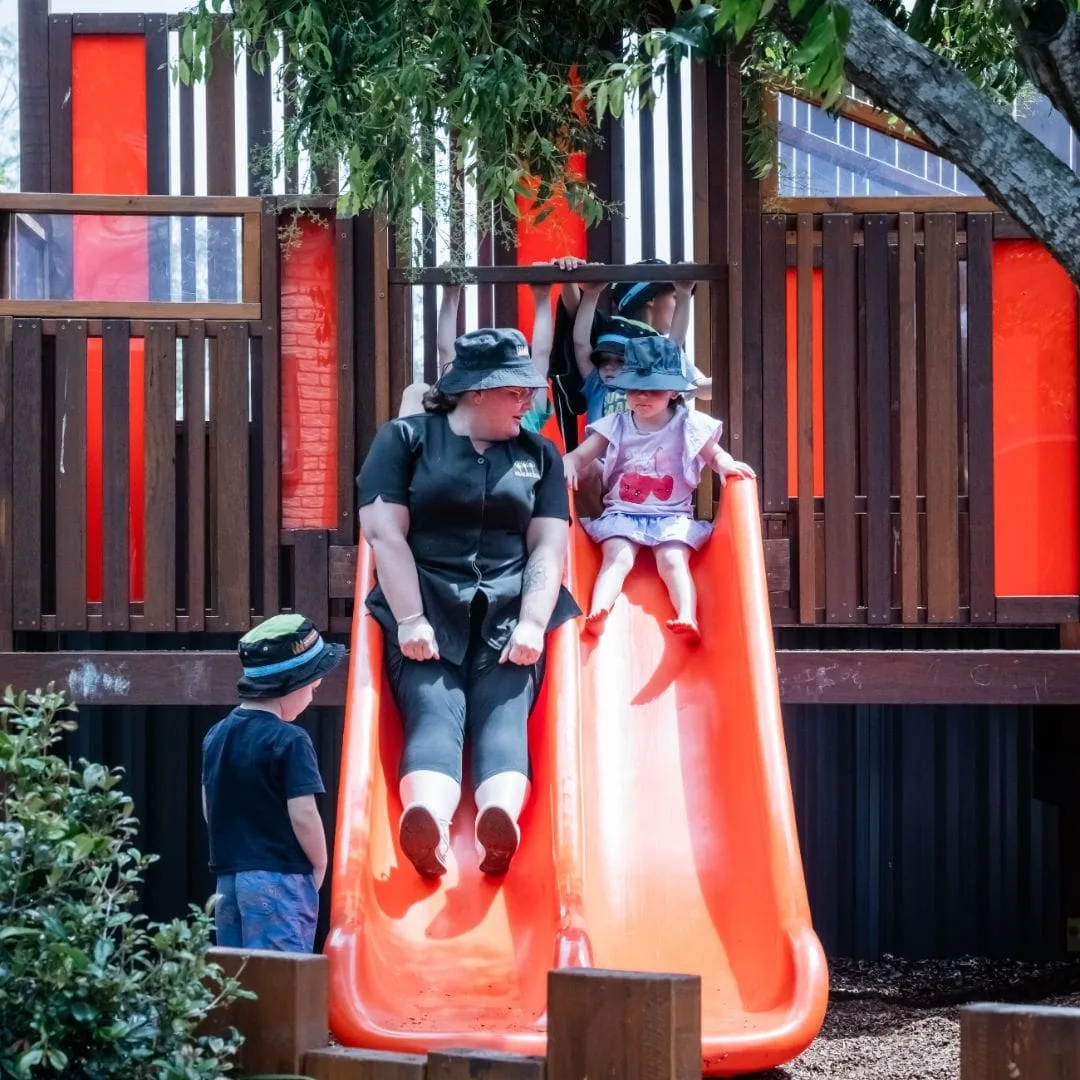 Educator and children sliding together on the playground slide